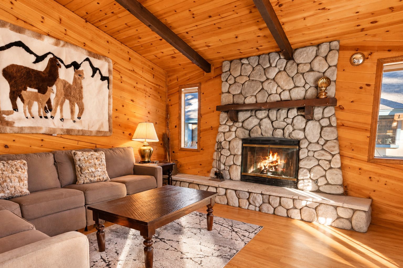 A cozy cabin interior with a stone fireplace, wooden walls, a sofa, and a rug.