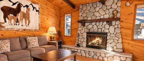 A cozy cabin interior with a stone fireplace, wooden walls, a sofa, and a rug.