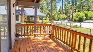 A wooden deck with metal chairs and a table, overlooking a fenced yard with trees. - The Great Escape (Big Bear City)
