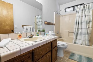 Un baño con tocador de madera, inodoro, ducha con cortina escocesa y espejo.