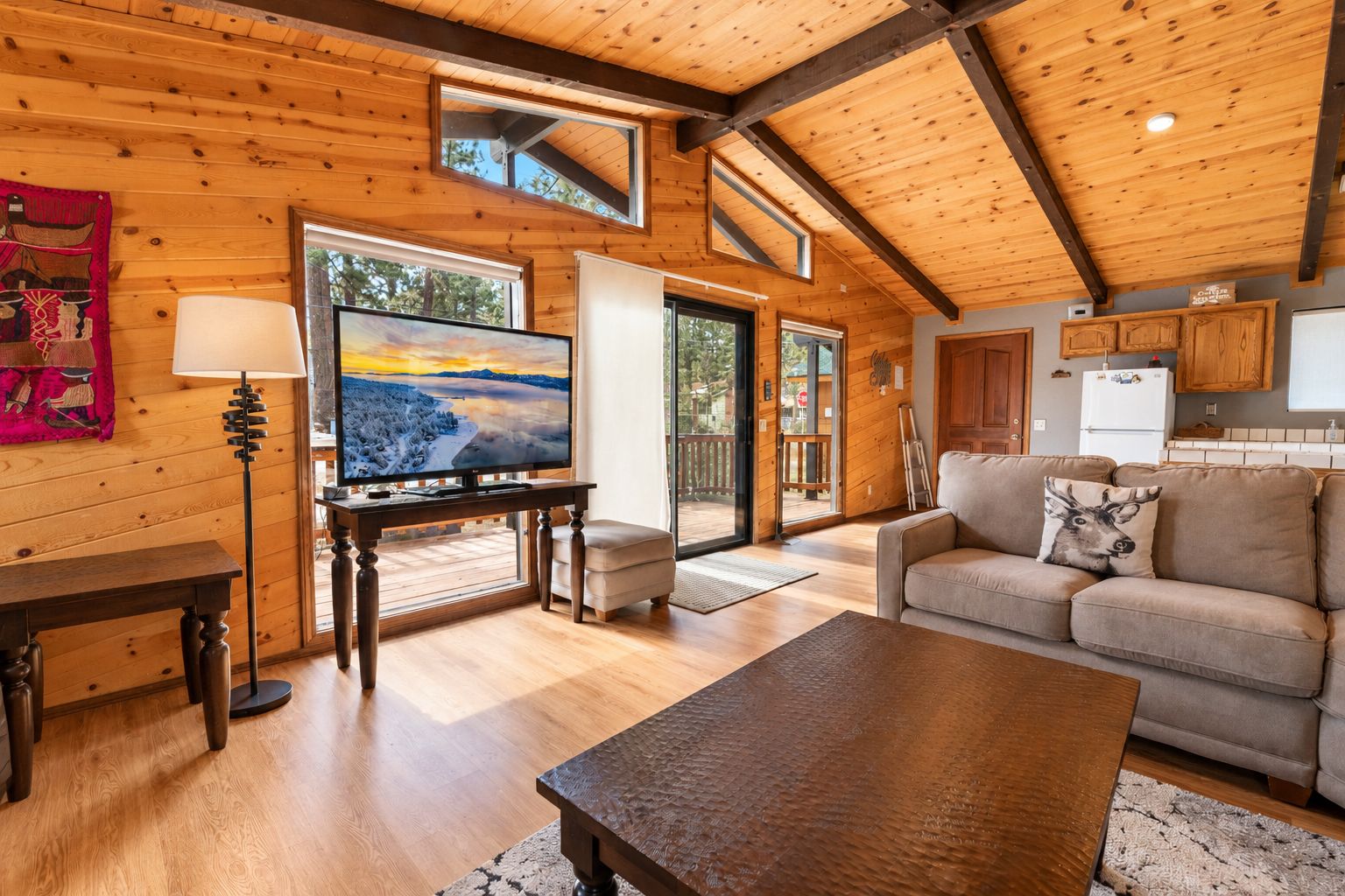 L’intérieur chaleureux d’un chalet avec un plafond en bois, une télévision, un canapé et une table à manger.