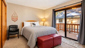 A bedroom with a bed, a chair, a red ottoman, a lamp, and a view of a balcony with a railing. - The Great Escape (Big Bear City)