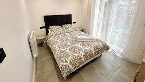 Ein Schlafzimmer mit Bett, Heizkörper, einem Fenster mit Vorhängen und Blick ins Freie.