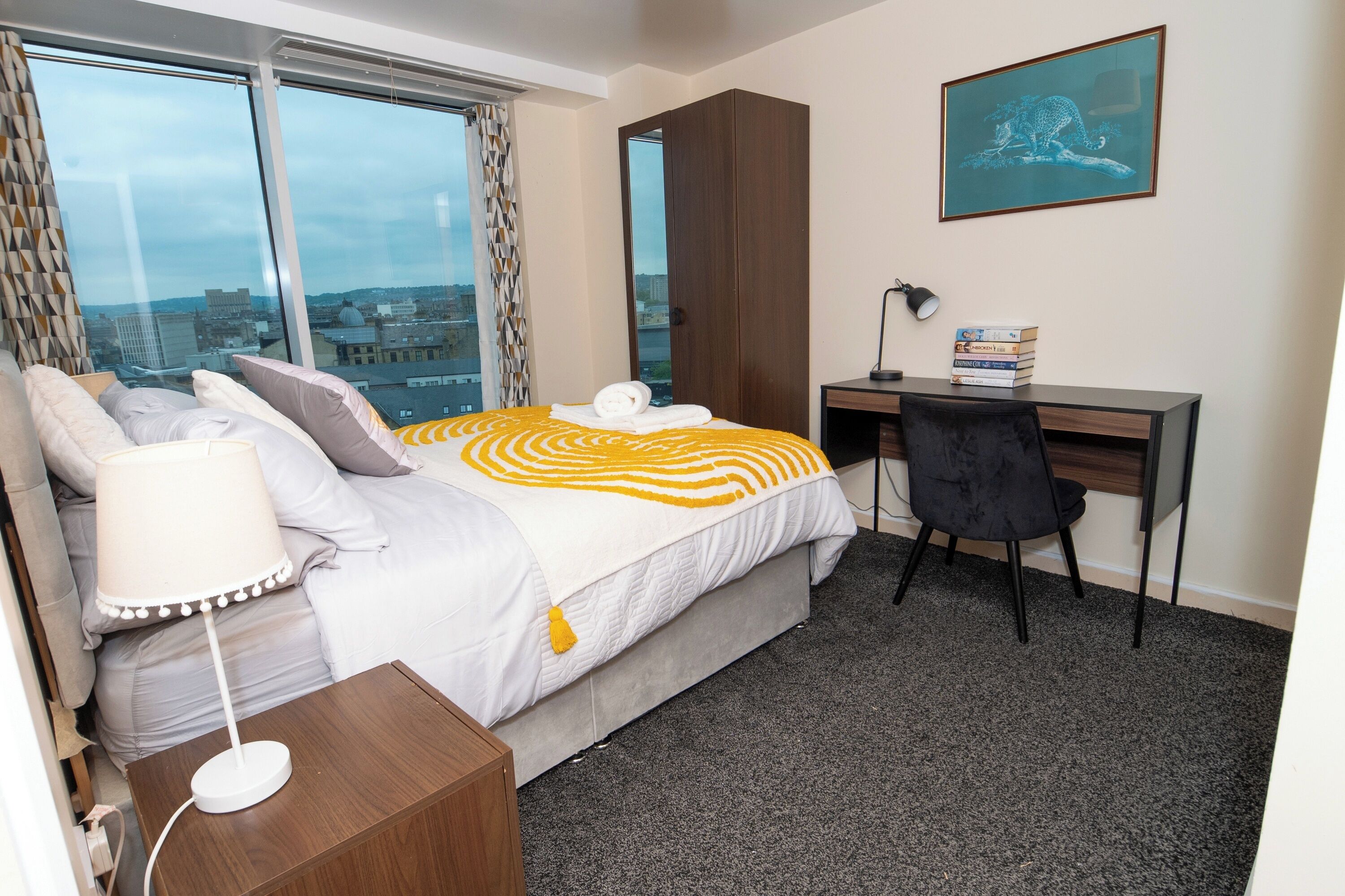 Ein Hotelzimmer mit Bett, Schreibtisch, Stuhl, Lampe und Blick auf die Stadt.