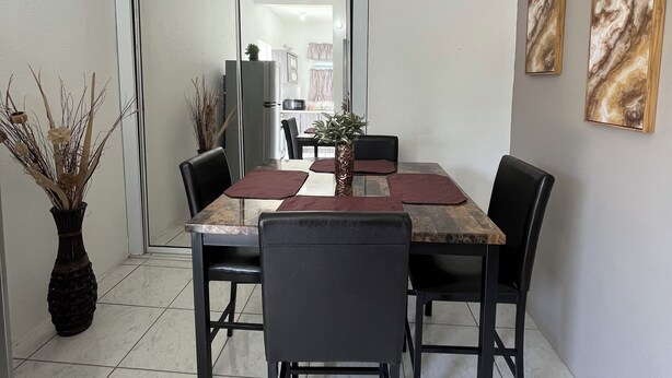 Un comedor con una mesa y sillas, un florero con plantas secas y dos cuadros abstractos en la pared.