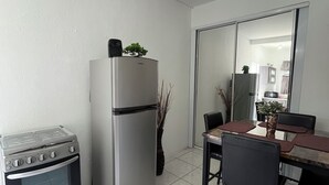Cocina compacta con estufa, horno y refrigerador. Hay una mesa de comedor con sillas y una planta en maceta.
