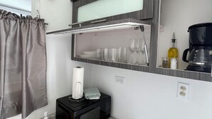 Una cocina compacta con un lavamanos, un microondas, una pequeña estantería con cristalería y una cafetera.