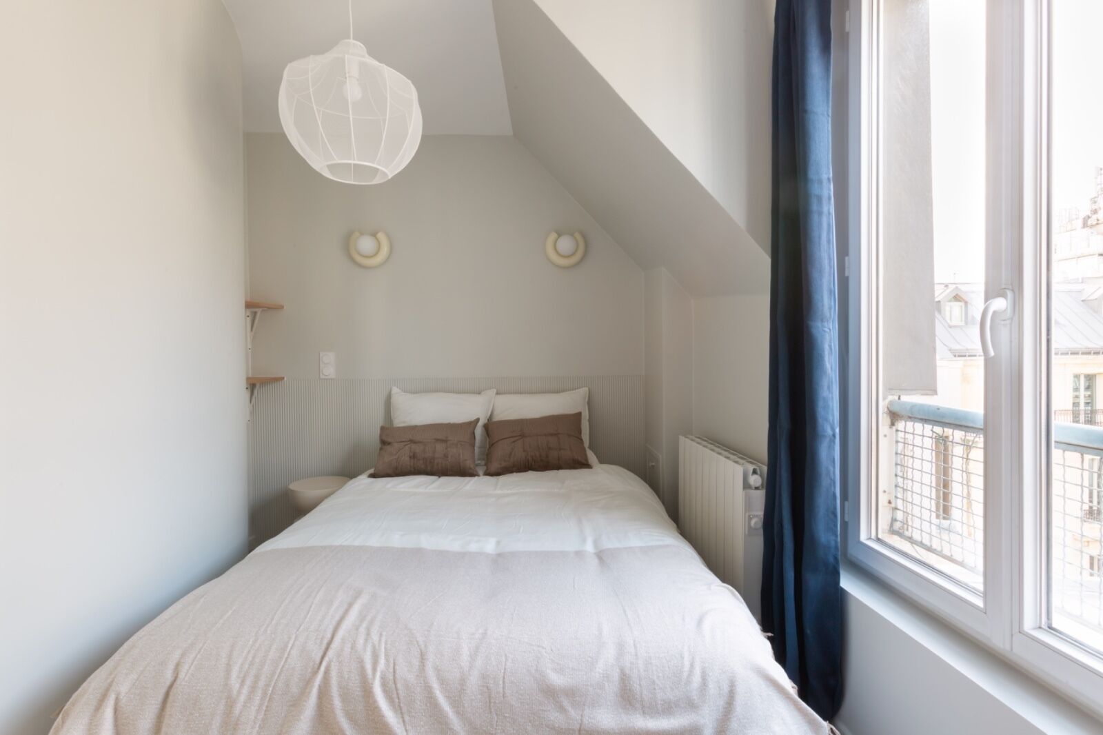A bedroom with a bed, a radiator, a window with curtains, and a hanging light fixture.