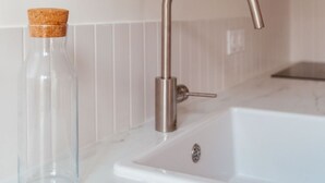 A kitchen with a white marble countertop, a stainless steel faucet, and a clear glass bottle with a cork stopper. - The (Courdemanche)