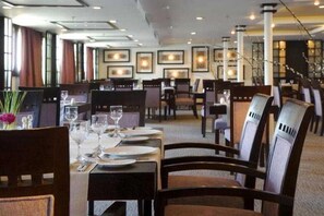 Un restaurant où les tables sont dressées pour le service, où des œuvres d’art encadrées ornent les murs et où l’éclairage intérieur crée une ambiance chaleureuse.