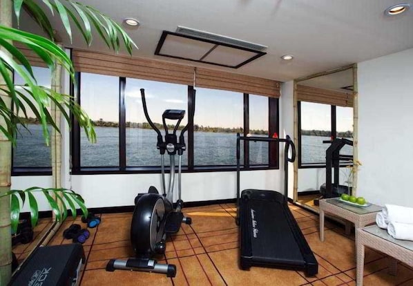 A gym with exercise equipment, a treadmill, and a view of a body of water through large windows.