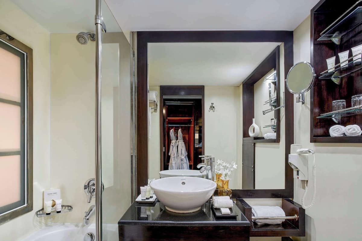 A modern bathroom with a large white sink, a bathtub, and a vanity with a mirror and towel rack.