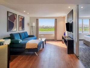 Habitació d'hotel moderna amb un sofà gran, una televisió i vistes a un paisatge verd.
