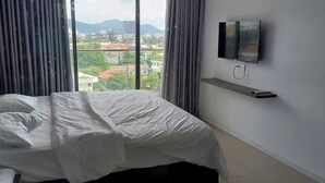 A hotel room with a bed, a TV mounted on the wall, and a view of the cityscape. - Premium CSJ Apartment - Nice View and Walk To Vung Tau Beach (Vũng Tàu)