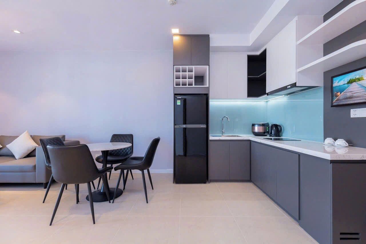 Une cuisine moderne dotée d’un réfrigérateur encastré, un coin repas avec une table et des chaises, et un canapé dans l’espace salon.