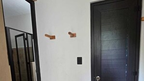 Un corridoio con una porta in legno scuro, un muro bianco e una piccola mensola in legno.