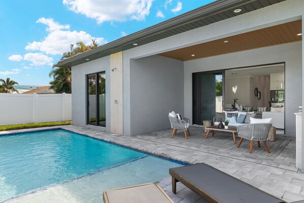 Ein moderner Poolbereich im Freien mit überdachter Terrasse, Sitzgelegenheiten und Blick auf die umliegende Landschaft.