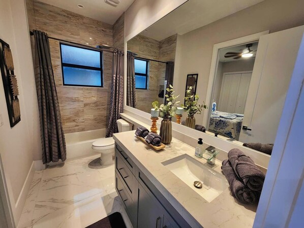 A modern bathroom with a large mirror, a bathtub, a toilet, and a vanity with a sink and towel rack. - Luxury Suites: Pool:Fast Internet: Close to Beach (Naples)