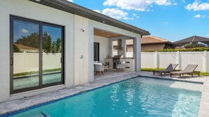 Une maison moderne dotée d’une piscine, d’une terrasse avec des chaises et d’un espace barbecue.