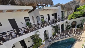 En moderne resort med en central swimmingpool, flere balkoner og frodig vegetation.
