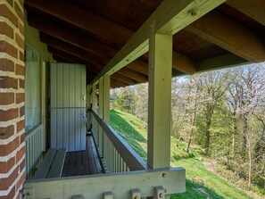 A covered porch with a wooden floor and white railings, overlooking a grassy hillside with trees. - 4 Star Holiday Home in Allinge (Allinge)
