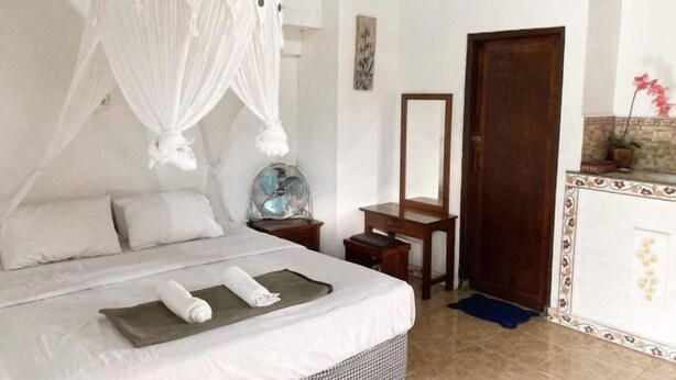 A bedroom with a canopy bed, a bedside table with a lamp, a mirror, and a wooden door. - Taman Ayu Homestay Munduk Mitra RedDoorz (Bali)