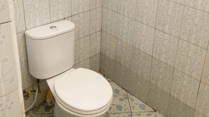 A small bathroom with a toilet, tiled walls, and patterned floor tiles. - Taman Ayu Homestay Munduk Mitra RedDoorz (Bali)
