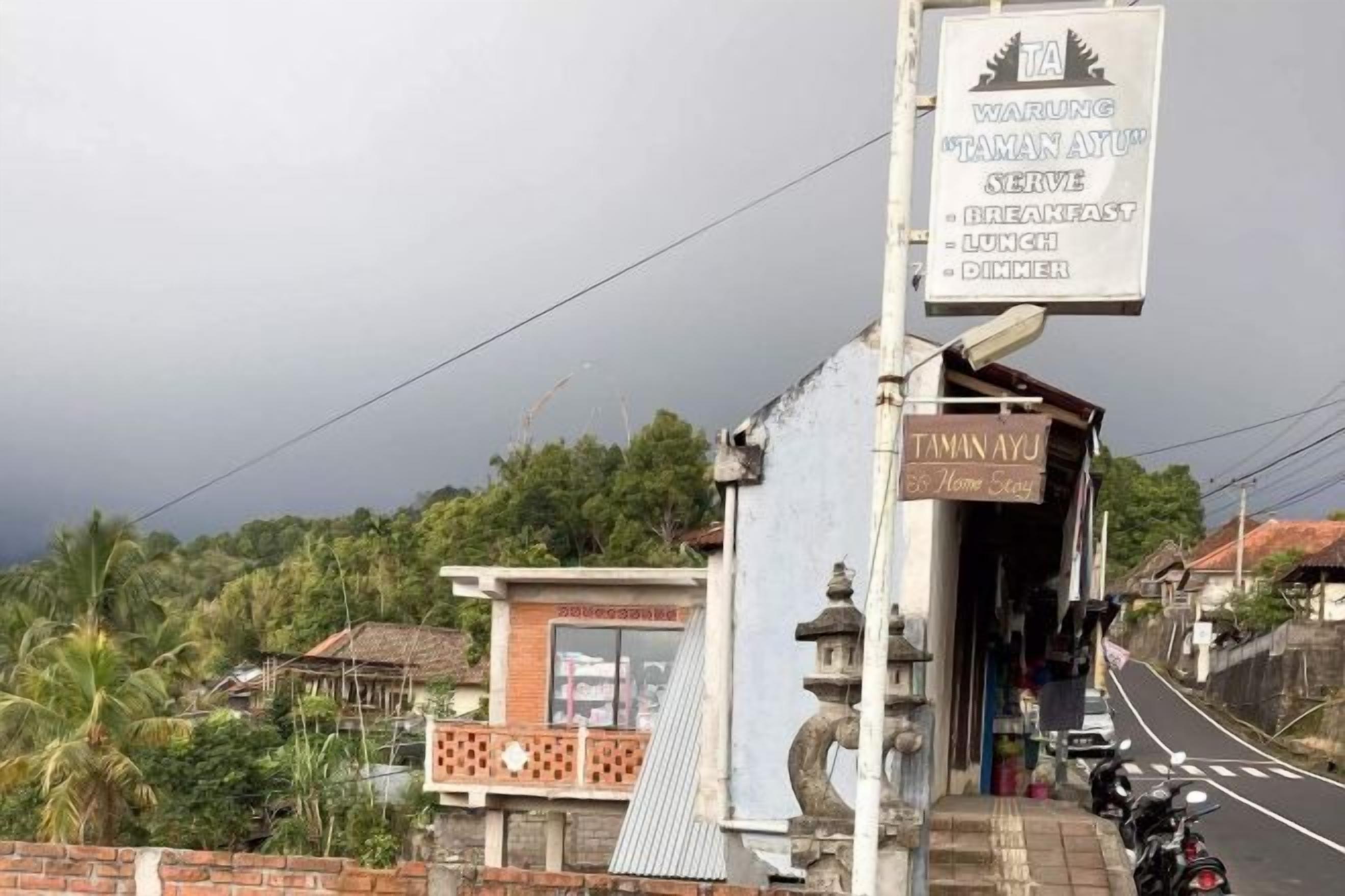 Un letrero para un restaurante llamado 'TAMAN AYU' con una lista de horarios de comida.