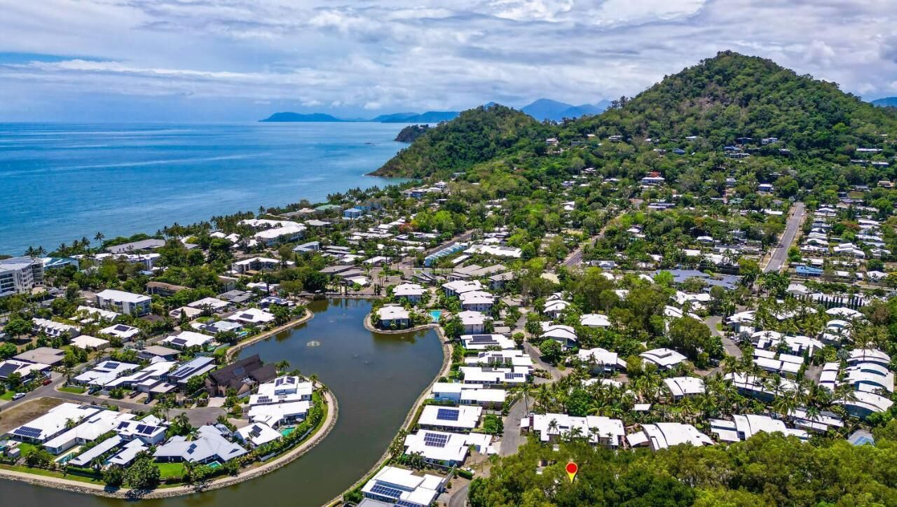 An aerial view of a coastal resort with multiple bungalow-style accommodations, a central water feature, and lush greenery.