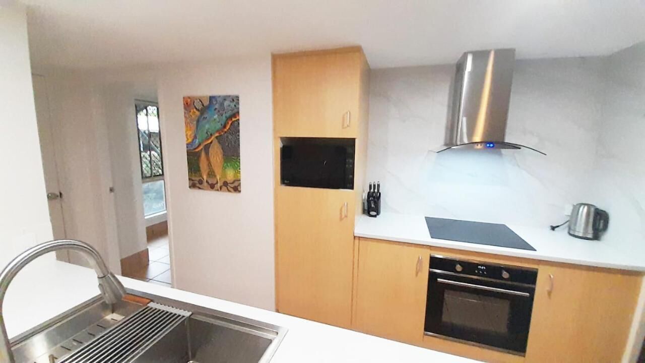 Una cocina compacta con un lavamanos de acero inoxidable, un microondas, una estufa y una campana extractora. Hay una pequeña ventana y un cuadro en la pared.