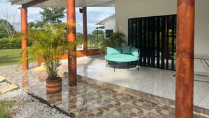 A covered outdoor area with a tiled floor, a teal sofa, and a potted plant.