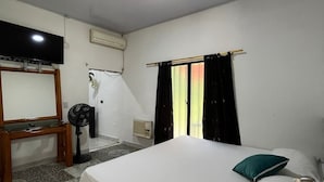 A bedroom with a bed, a TV, a fan, and a window with curtains.