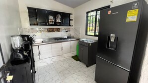 A compact kitchen with a black refrigerator, a stove, and a blender.