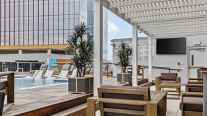 Ein Poolbereich auf dem Dach mit Holzmöbeln, einem Pool und einem modernen Gebäude im Hintergrund.