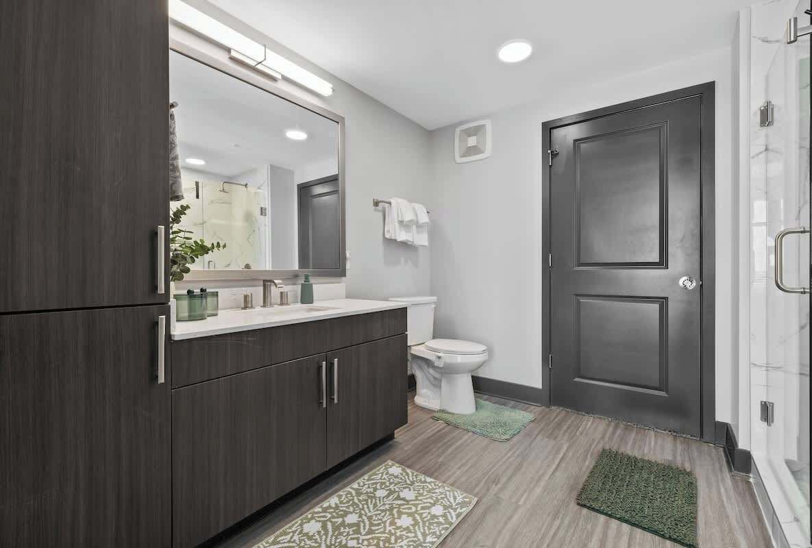 A modern bathroom with dark wood cabinets, a white toilet, and a glass shower enclosure.