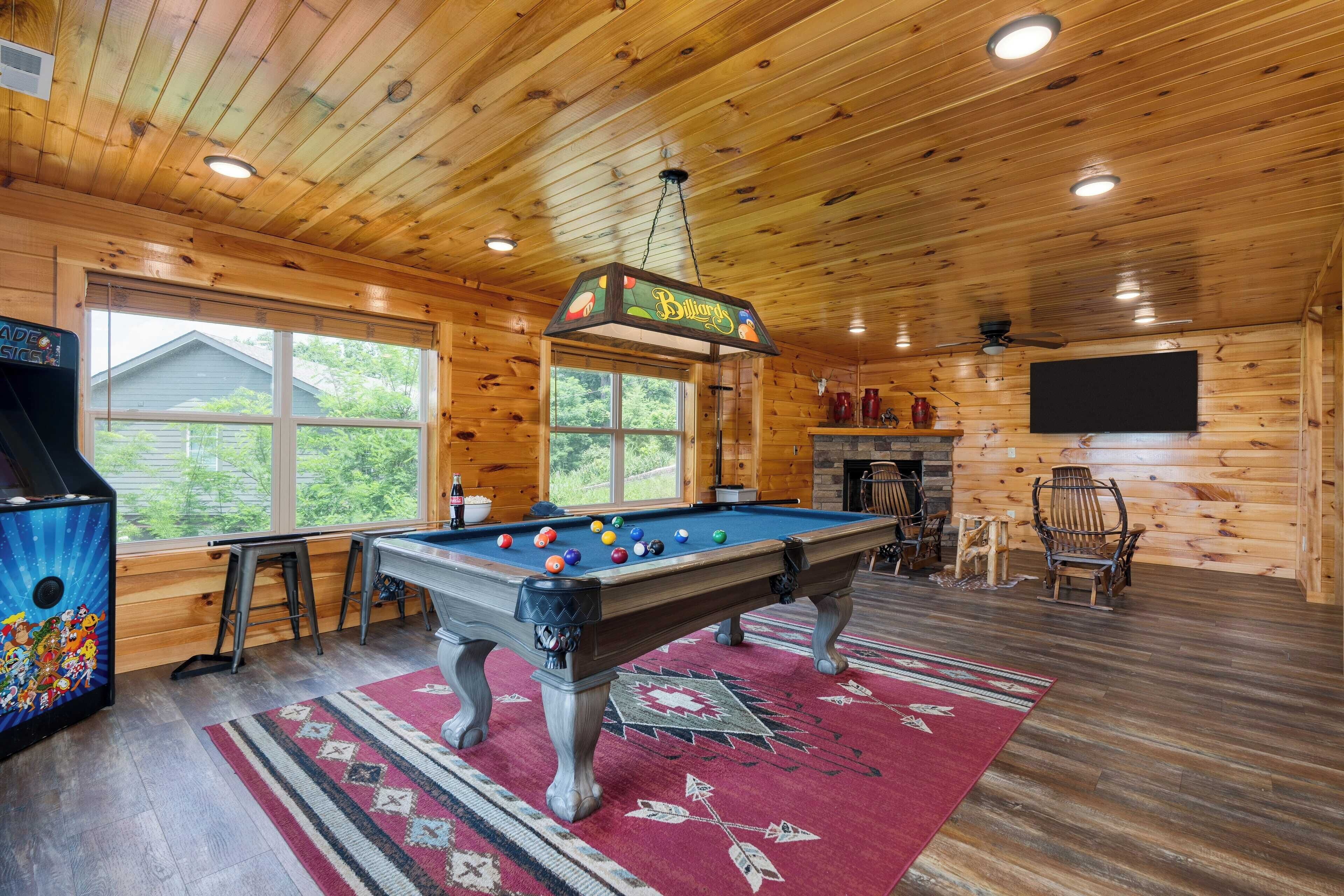 A wooden cabin interior with a pool table, a dartboard, and a television mounted on the wall.