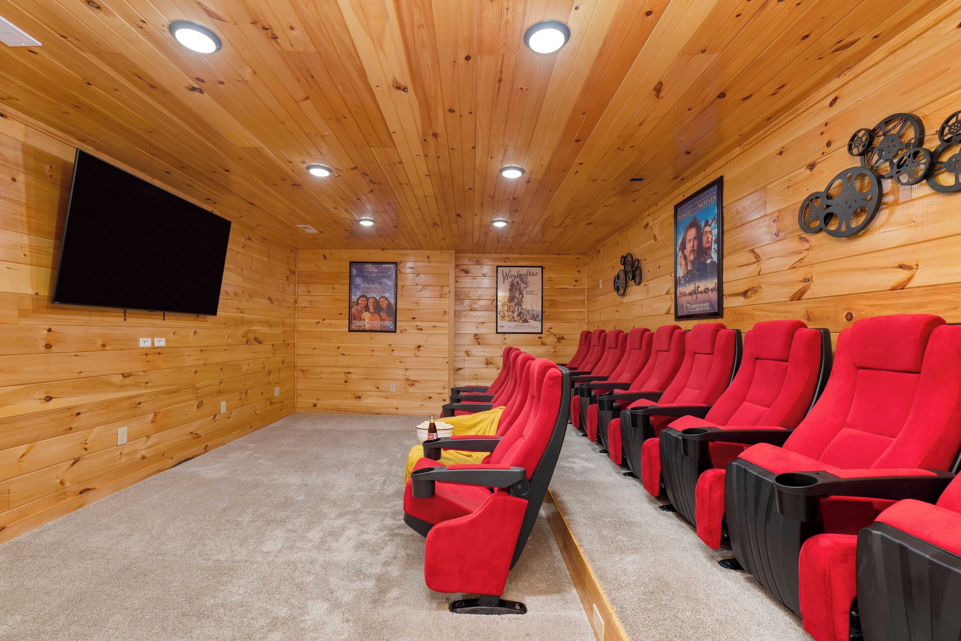 A cinema room with wooden walls, red and black seating, a large screen, and a poster on the wall.