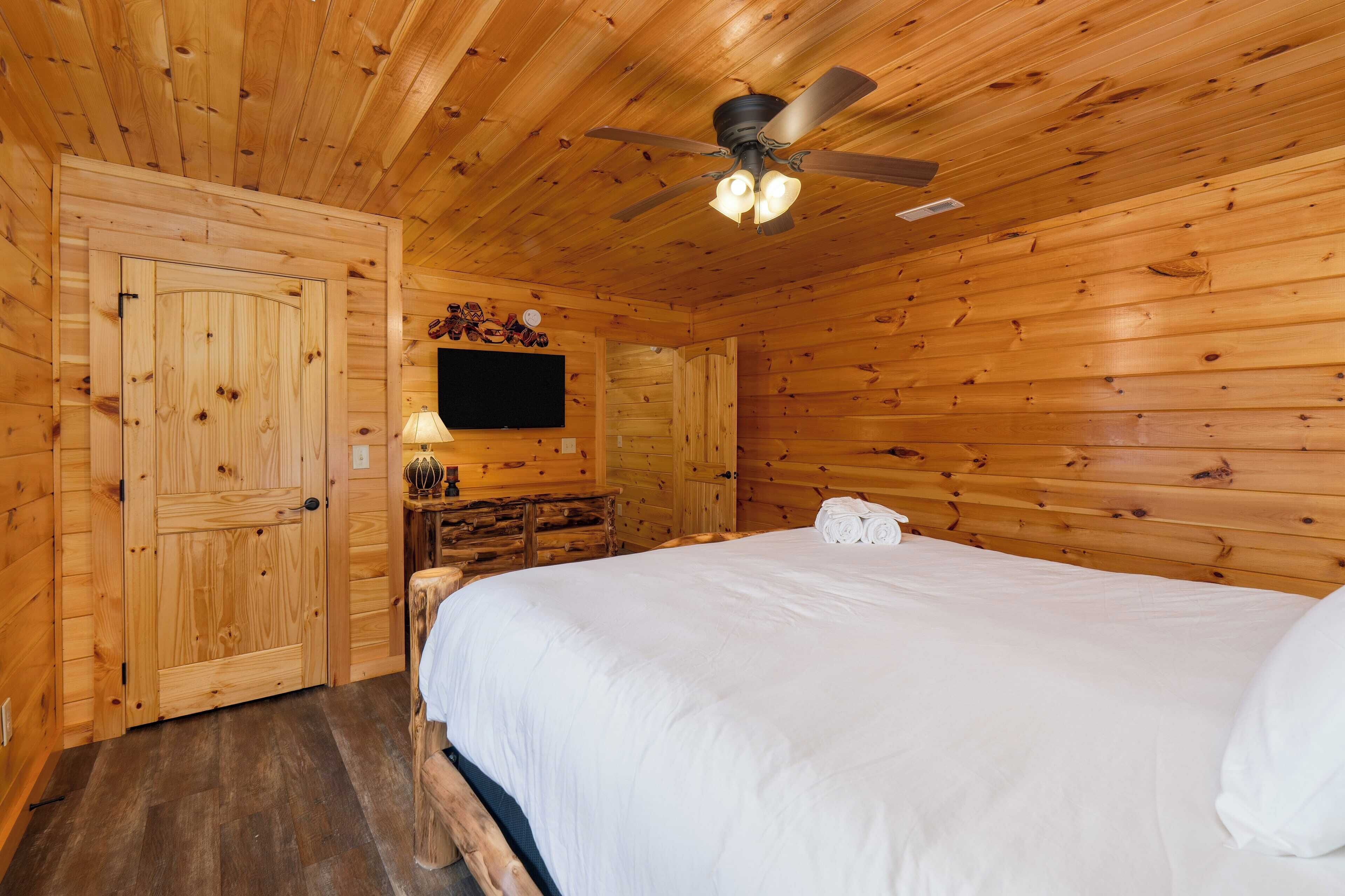 A wooden-paneled room with a bed, a ceiling fan, and a flat-screen TV mounted on the wall.