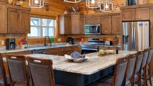 A spacious kitchen with wooden cabinets, a large island with chairs, a refrigerator, and a microwave. - Evergreen Echo by Avantstay Cabin w/ Mountain Views, Theater, Game Room, and Hot Tub (Gatlinburg)