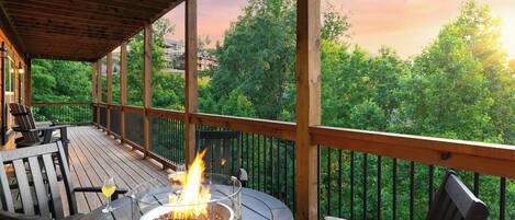 Terraza de madera con un hogar, asientos al aire libre y vistas a un bosque.