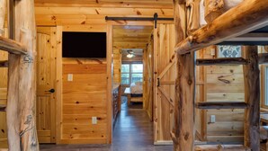 A wooden cabin interior with a bed, a bench, and a TV mounted on the wall. - Evergreen Echo by Avantstay Cabin w/ Mountain Views, Theater, Game Room, and Hot Tub (Gatlinburg)