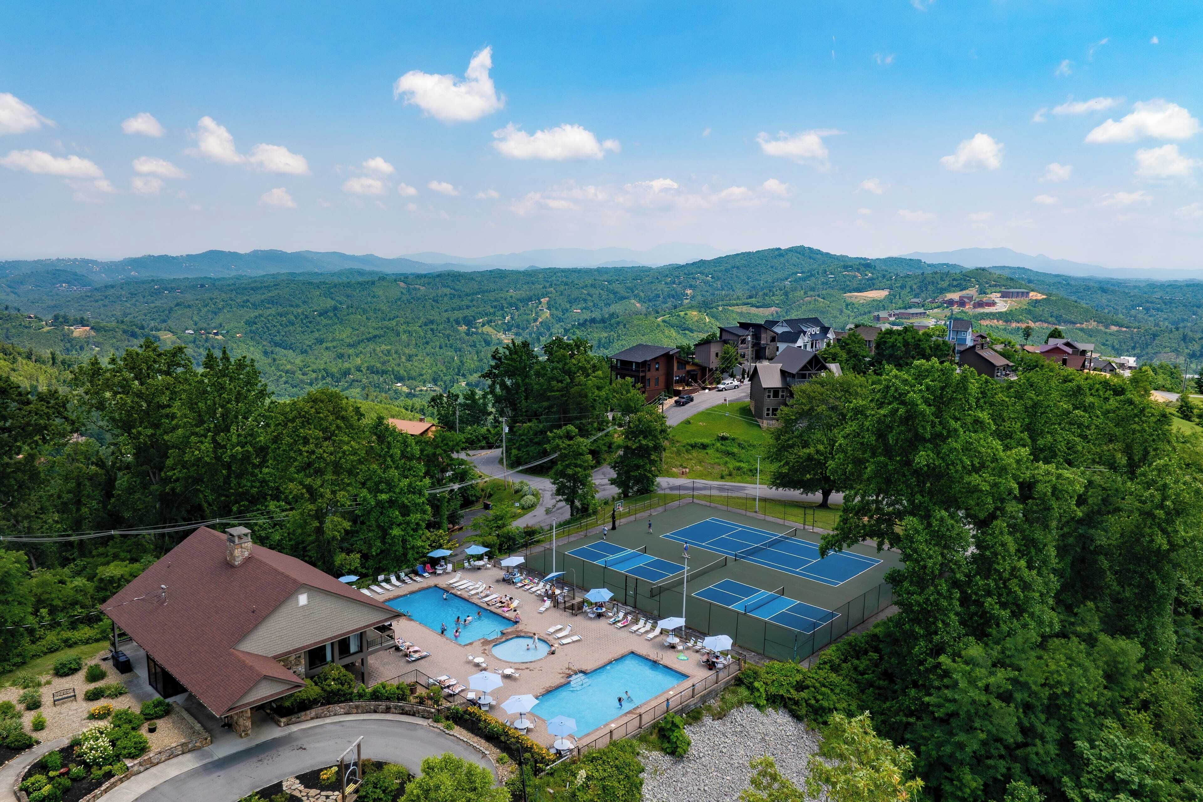 A resort with a swimming pool, tennis courts, and a view of the surrounding mountains.
