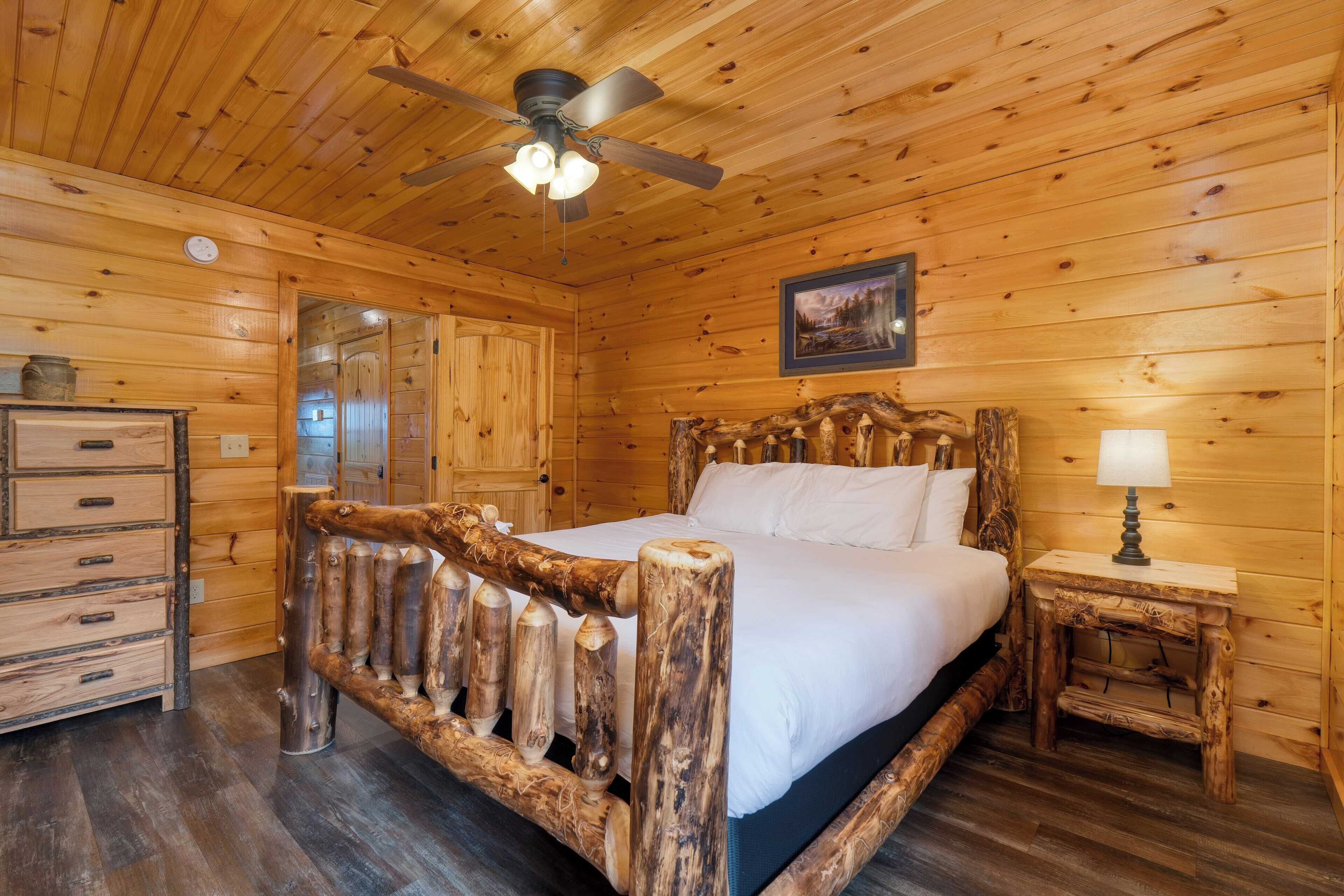 A wooden cabin bedroom with a bed, a nightstand, a dresser, and a ceiling fan.
