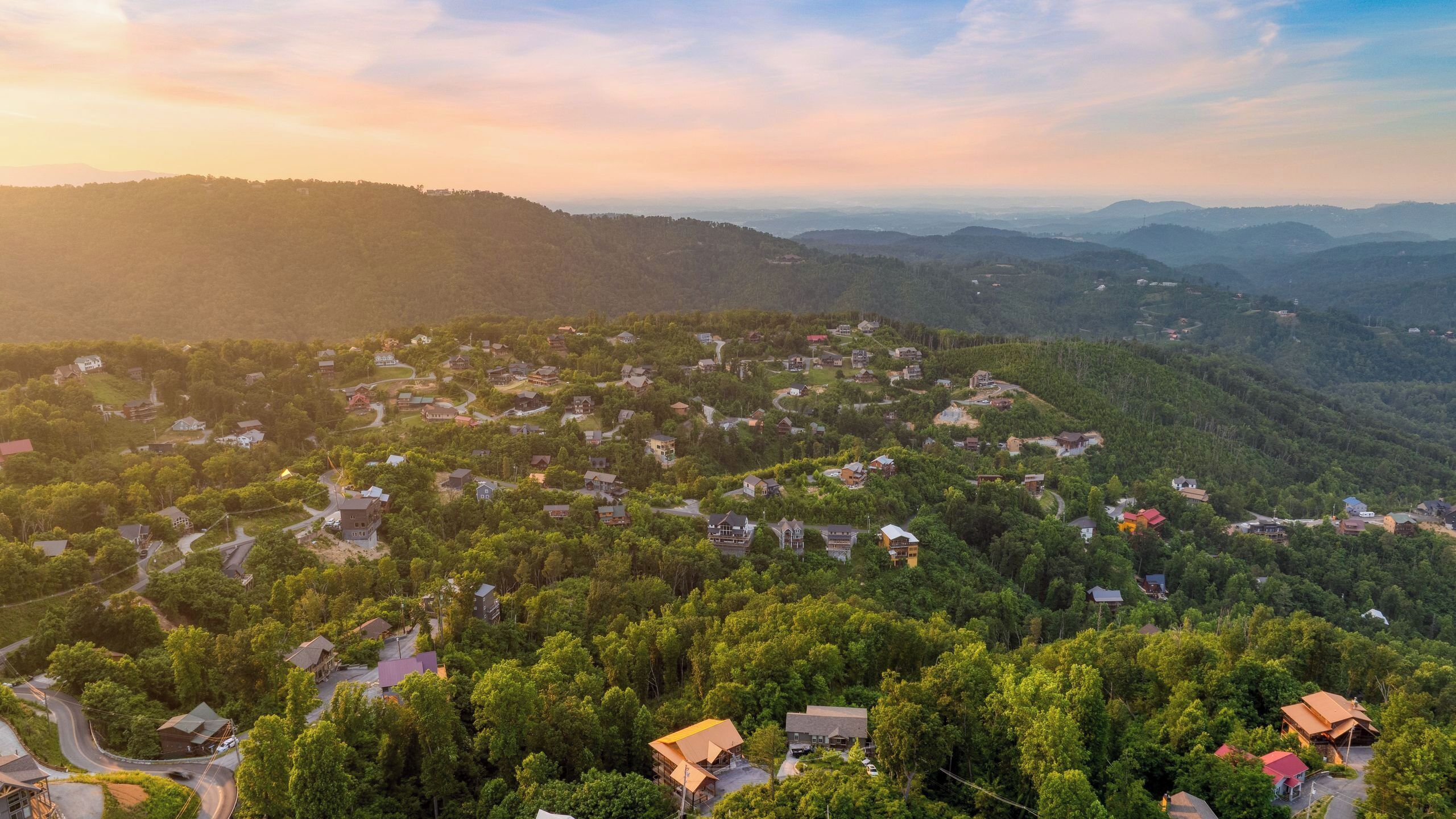 Un quartier résidentiel où les maisons sont entourées d’une forêt dense, de routes et d’un paysage vallonné.