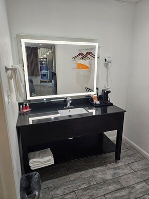 A bathroom with a black vanity, a large mirror, a towel rack, a hairdryer, and a trash bin. - The Edyn Hotel (Wytheville)
