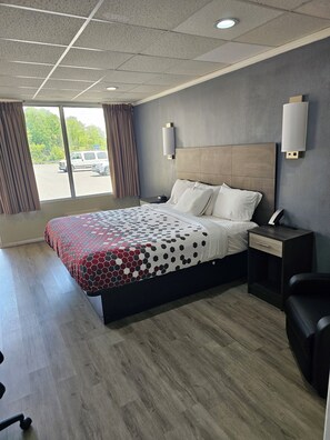 A hotel room with a large bed, a nightstand, a desk, and a chair. There is a window with curtains and a view of the outside. - The Edyn Hotel (Wytheville)