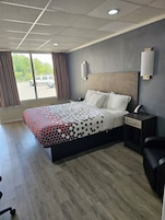 Habitación de hotel con una cama grande, una mesita de noche, un escritorio y una silla. Hay una ventana con cortinas y vistas al exterior.