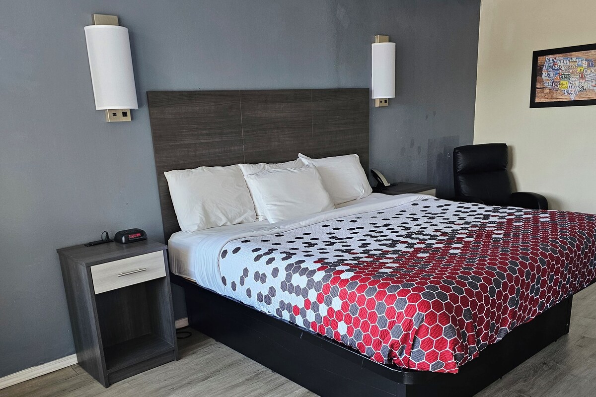 A modern hotel room with a large bed, a nightstand, a desk, and a chair.