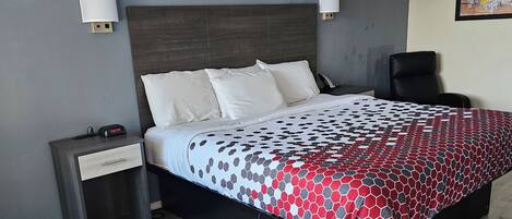 A modern hotel room with a large bed, a nightstand, a desk, and a chair.