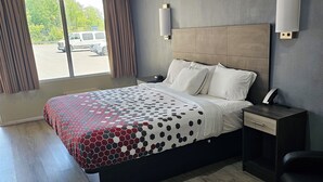 A hotel room with a large bed, a nightstand, a desk, and a chair. There is a window with curtains and a view of the outside. - The Edyn Hotel (Wytheville)